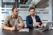 © Liubomir - Two business colleagues collaborate, using a laptop and tablet to review documents and discuss ideas at their office table.