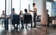 © Prostock-studio - Modern Corporate Meeting Concept. Young Businessman In Medical Face Mask Giving Speech During Meeting With Coworkers In Office, Standing At Table In Board Room, Explaining Strategy And Management