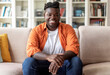 © Prostock-studio - Portrait of happy handsome young black man in casual outfit with braids sitting on couch at home, smiling at camera, living room interior, copy space. Millennials lifestyles concept