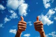© dgete - Two hands showing thumbs up gesture against a bright blue sky with scattered white clouds conveying positivity and approval