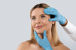 © Prostock-studio - Plastic surgery or face lifting for middle aged woman. Doctor hands wearing blue medical gloves holding head of female patient, checking skin before procedure, isolated on grey background, copy space