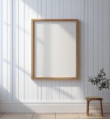 Aufkleber - Minimalist interior with blank wooden frame hanging on white paneled wall, sunlight casting soft shadows, small wooden stool with green plant beside it
