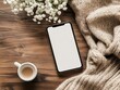 © Selsi - Flat lay of a smartphone with blank screen, coffee, flowers, and a knit sweater on a wooden surface