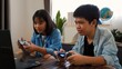 © FAMILY STOCK - Asian teenage boy and girl playing video games at home together. Concept of digital lifestyle, esports, fun learning, teamwork, and modern entertainment for kids and teens indoors.