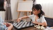 © FAMILY STOCK - Two Asian sisters playing chess at home, developing brain skills, logical thinking, and bonding through fun strategic games in a cozy indoor learning environment.