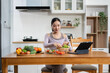 © NINENII - Fit woman enjoys healthy fresh vegetables and fruits breakfast sitting in the kitchen.