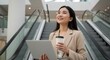 © Azis Stock - Businesswoman using laptop on escalator, enjoying coffee break