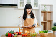 © laddawan - Asian woman preparing healthy food with smartphone in home kitchen. Great for wellness, clean eating, cooking content