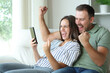 © Antonioguillem - Excited couple checking mobile phone sitting in a sofa