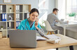 © Studio Romantic - Friendly female nurse receptionist answering telephone call, sitting at desk with laptop computer, scheduling appointments, writing down notes in notebook, posing in medical clinic