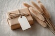 © sukarman - A gift-wrapped box of kraft paper, tied with light brown twine, sits on a light beige craft paper background. A simple white  tag hangs from the twine.