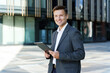 © muse studio - Business professional engages with digital device outside a modern office building in bright sunlight