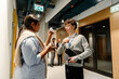 © Drobot Dean - A young White man and a young Indian woman standing and discussing documents inside a hallway, both wearing business clothes, holding papers and notebooks, and having a conversation during work.