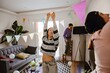 © Drobot Dean - Three young, Asian and brown-skinned female friends decorate the living room for a party together, inflating balloons and hanging garland. A concept of teamwork, girlhood, and partying.