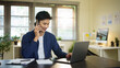 © matinee - Young businessman smiling while having a phone conversation and working on a laptop in modern office.