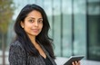 © banrak - Portrait of a successful Indian female executive using a touchscreen tablet in front of a modern commercial building