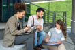 © Srdjan - Diverse team of corporate professionals in formal attire collaborating outdoors, engaged in strategic discussion while analyzing data on laptop in front of modern glass office building.