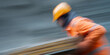 © Mind - Worker in motion wearing orange jacket and helmet, blurred background