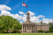 © lucky-photo - The Old Main building on the campus of Penn State University and American flag in spring sunny day, State College, Pennsylvania.