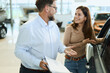 © Goran - Happy salesman selling the car to his female customer in a showroom.