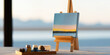© SnowElf - A small easel holds a canvas with a serene landscape painting, while paint containers rest nearby on a table. Art creation process, painting supplies