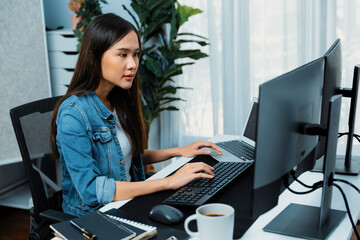 smiling young asian it developer working software development information on pc screens and laptop, 