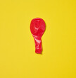 © nndanko - One red deflated balloon lies on a yellow background.