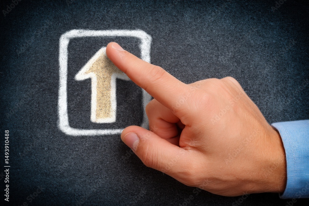 A hand with a light skin tone points at a chalk drawing of an upward arrow on a dark board. This moment captures creativity and intention, highlighting a dynamic learning or brainstorming environment.