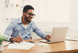 © Prostock-studio - Happy black businessman working on laptop in modern white office interior. Smiling employee at work with computer, copy space