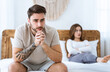 © Prostock-studio - Impotence concept. Sad man presses hands to his chin and ponders, wife disappointed folded arms at bed, at interior