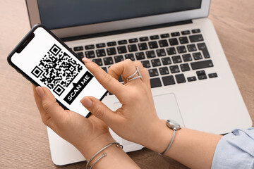 Woman holding smartphone with QR code on screen at table, closeup