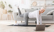 © Prostock-studio - Fitness at home. Sporty senior woman exercising in front of laptop in living room, watching online tutorials, doing workout for legs, free space