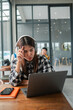 © Satori Studio - Focused young woman wearing headphones, working on a laptop in a contemporary cafe environment.