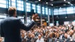 © Azorahaiá - A speaker addresses a large audience at a conference, gesturing with his hand. The room is well-lit and filled with people.