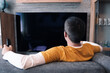 © diy13 - Male viewer in a yellow T-shirt against a black TV screen. Young handsome man watching TV on a sofa at home