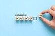 © All 1n One 😎 - Checklist and task progress tracking concept. A hand placing the final checkmark on wooden blocks in a progress bar, task completion, productivity, goal setting, and efficient project management.