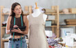 © JackF - Passionate young female seamstress concentrating on designing custom dress using tablet, reviewing and adjusting clothing model in well-equipped creative studio