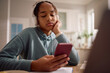 © Drazen - Displeased African American teenager girl using smart phone while learning at home.