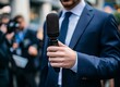 © ryanbagoez - Close-up of a reporter's microphone in the hands of a correspondent in a gray or dark blue suit