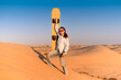 © EdNurg - Young woman enjoying the thrill of sandboarding in the sun soaked desert of Dubai, United Arab Emirates, surrounded by stunning dunes