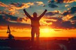 © Ann Studio - A construction worker with arms raised faces a vibrant sunset with construction equipment visible in the background.