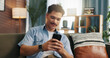 © peopleimages.com - Relax, smile and man with mobile on sofa for communication, chat and reading message. Home, online and happy person with smartphone for texting, social media and browsing website to download app