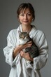 © Veronika - Woman in a robe holds a striped cat indoors during a cozy morning