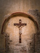 © MatyasSipos - A wooden crucifix depicting Jesus Christ is mounted on an arched, weathered stone wall inside a historic church in Grado, Italy. The worn textures reflect time and reverence.