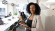 © fizkes - Portrait of African businesswoman standing in meeting room holds digital tablet, exuding professionalism and competence, colleagues or shareholders sit around conference table in background. Briefing