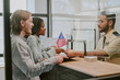 © AnnaStills - Diverse couple handing passports at immigration office counter with officer verifying documents and flag in background. Multi-ethnic group interacting in official setting