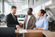 © Serhii - Car salesman explaining contract to african american couple in dealership