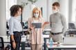 © Prostock-studio - Questions to manager during work. Woman boss in protective mask looks at tablet and checks task from guy and african american lady in interior of coworking office, panorama, free space