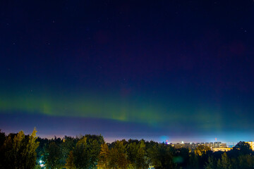 northern lights over city. pale light of aurora borealis in night sky. color flashes in northern hem