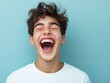 © Elegance Frames - A teenage boy laughing with a big open mouth, isolated on a light blue background